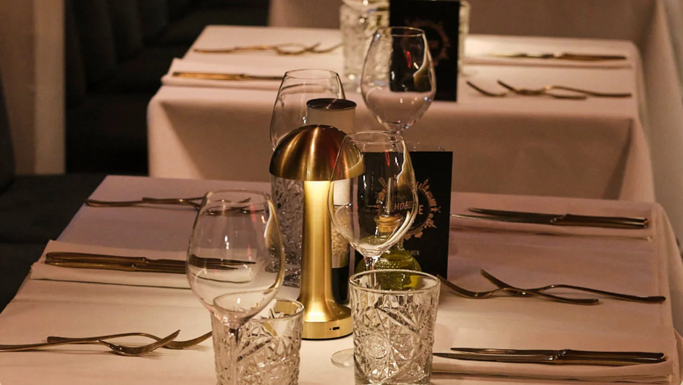 Gedekte tafels met kristallen glazen en een gouden tafellamp, in gedimd licht