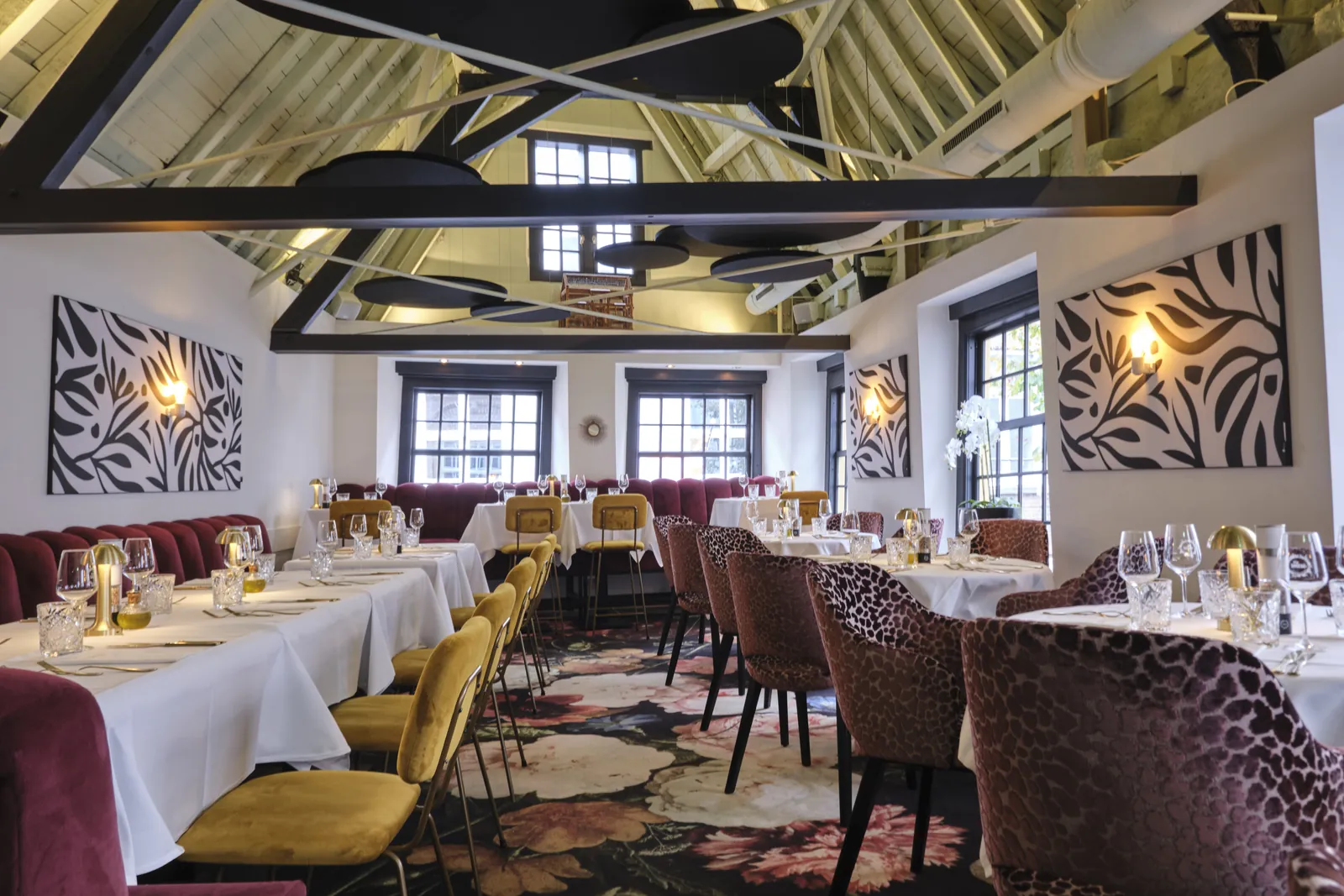 The LOFT onder de houten dakspanten, met zwarte ronde plafondeilanden boven de tafels